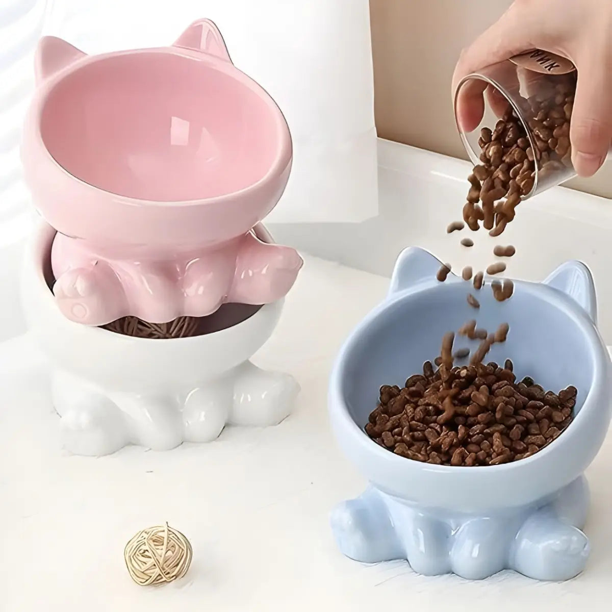 gamelle pour chat Cutie bleue et rose, remplissage de croquettes dans bol incline en ceramique.